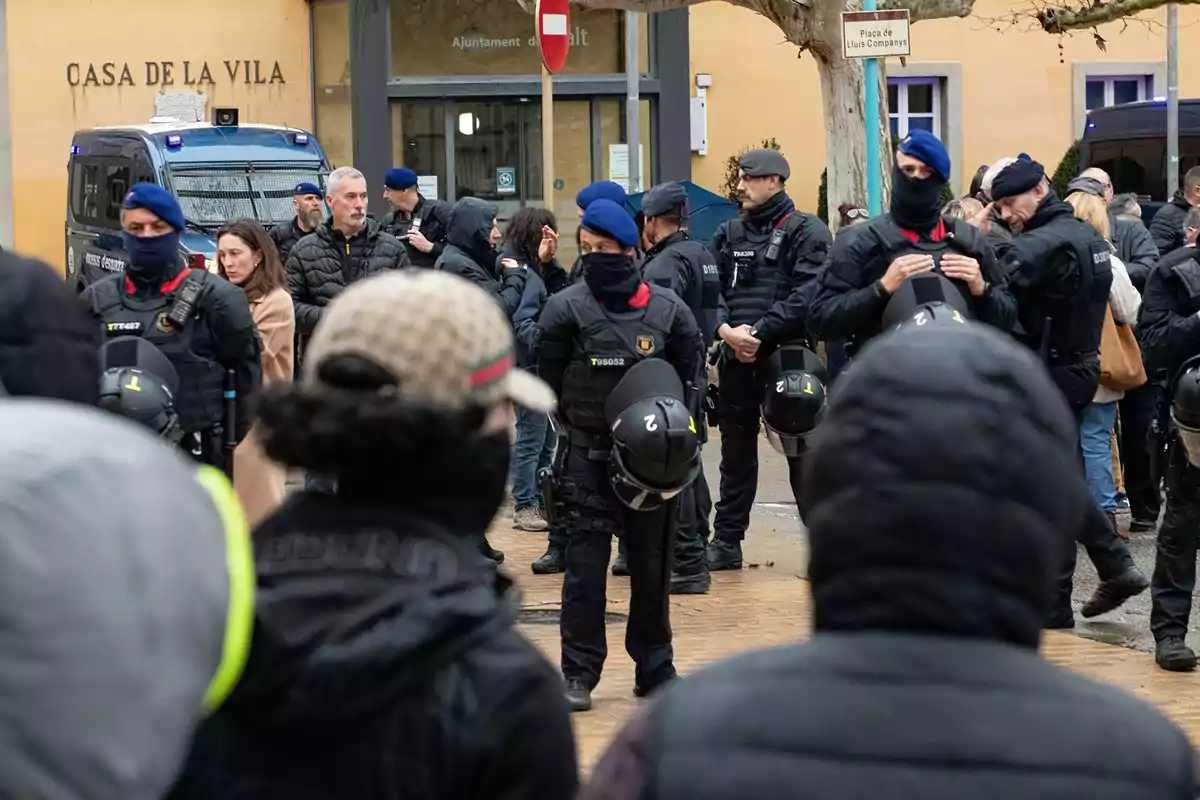 Un grupo de policías con equipo antidisturbios se encuentra en una plaza frente a un edificio con el letrero "Casa de la Vila", rodeados de personas vestidas con ropa de invierno.