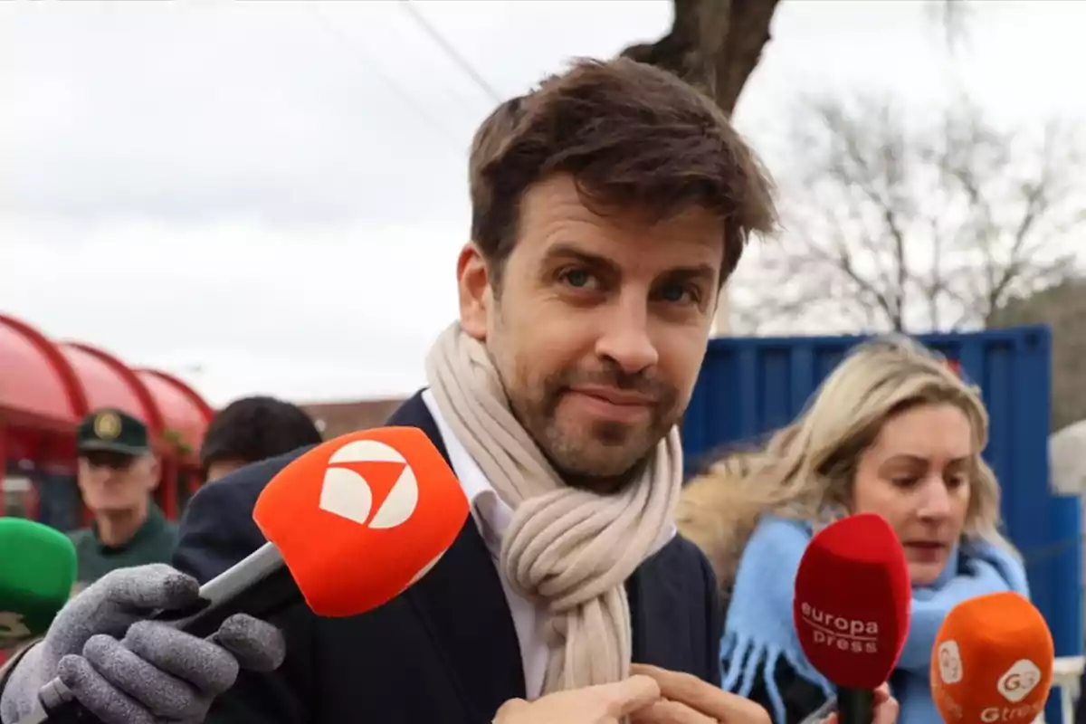 Un hombre con bufanda clara es entrevistado por varios medios de comunicación al aire libre.