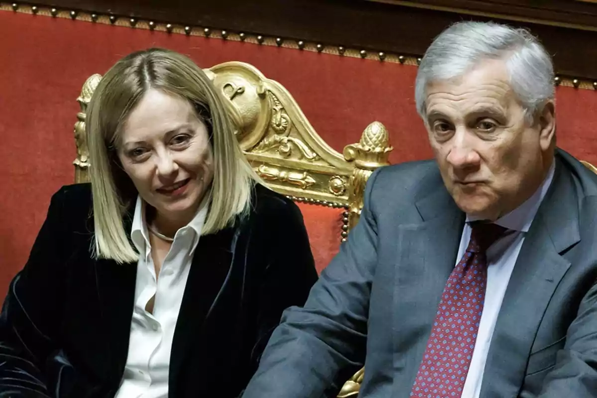Dos personas sentadas en sillas doradas con fondo rojo.