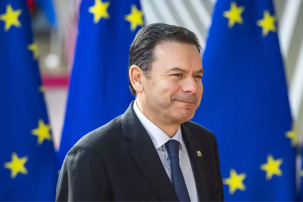 Un hombre con traje y corbata frente a banderas de la Unión Europea.