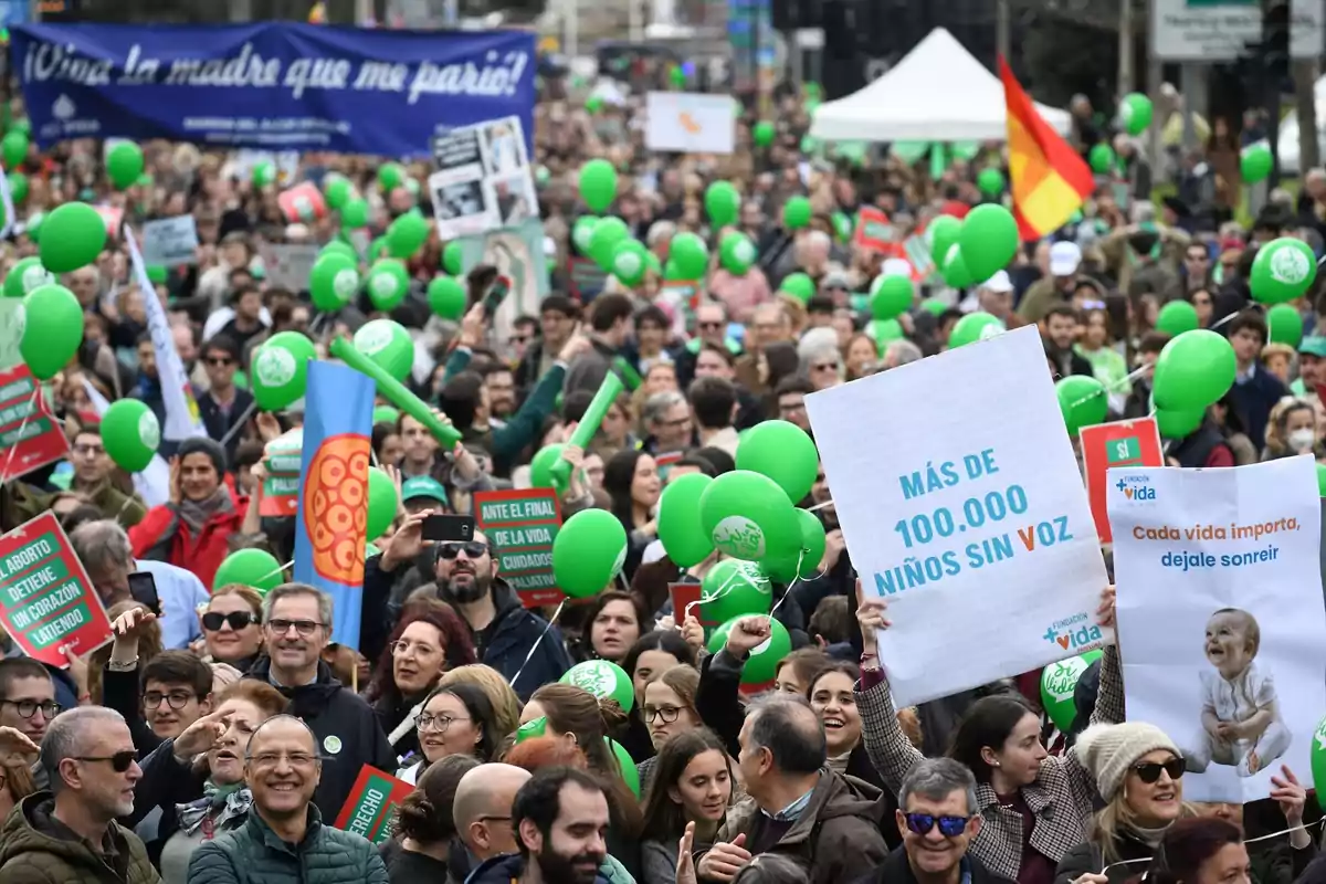 Una multitud de personas participa en una manifestación sosteniendo pancartas y globos verdes.