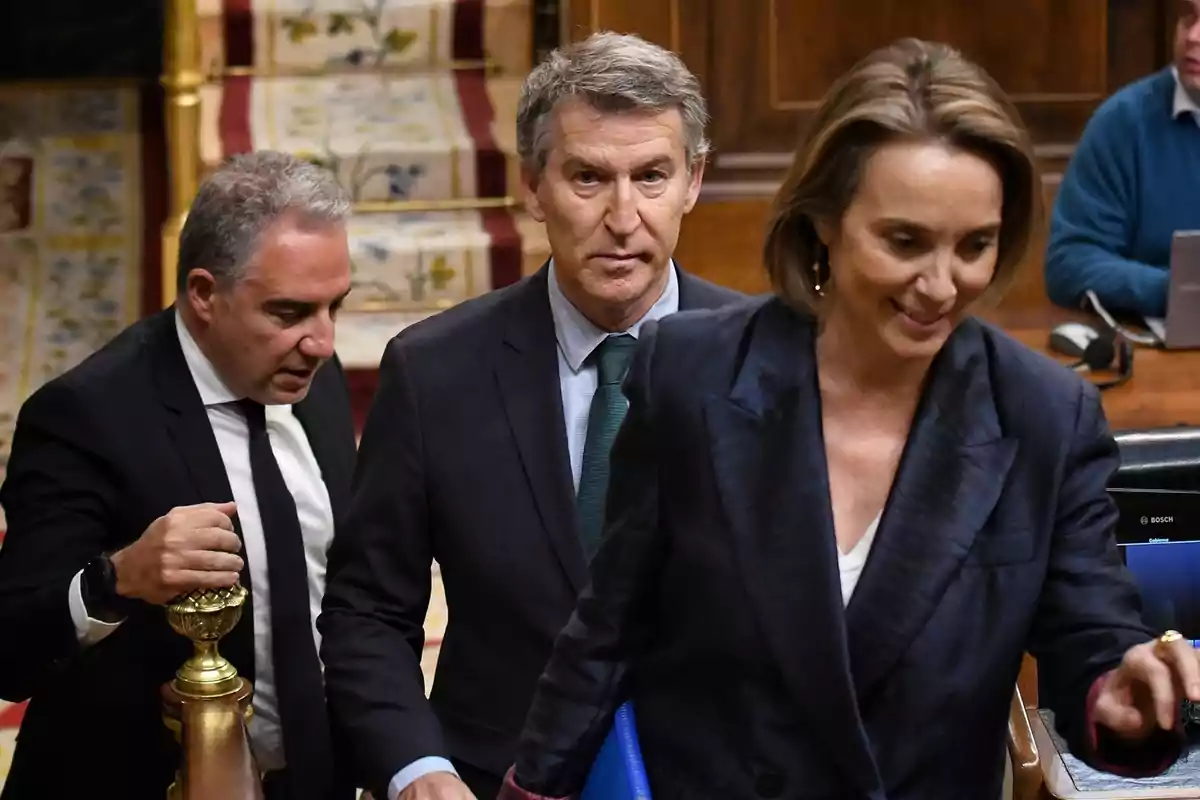 Un grupo de personas vestidas formalmente camina en un entorno interior con decoración elegante y un ambiente profesional.