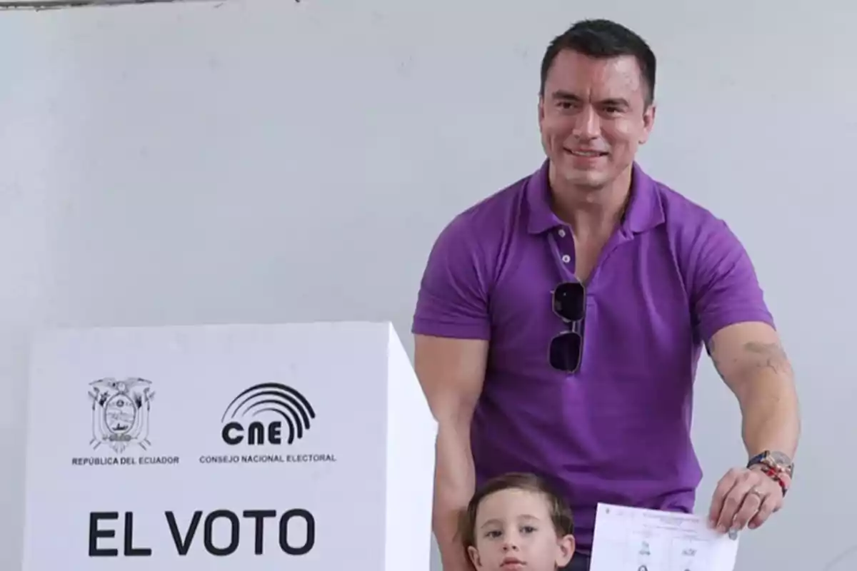 Un hombre con camisa morada y un niño pequeño están junto a una urna de votación en Ecuador, sosteniendo un documento. Un hombre con camisa morada y un niño pequeño están junto a una urna de votación en Ecuador, sosteniendo un documento.