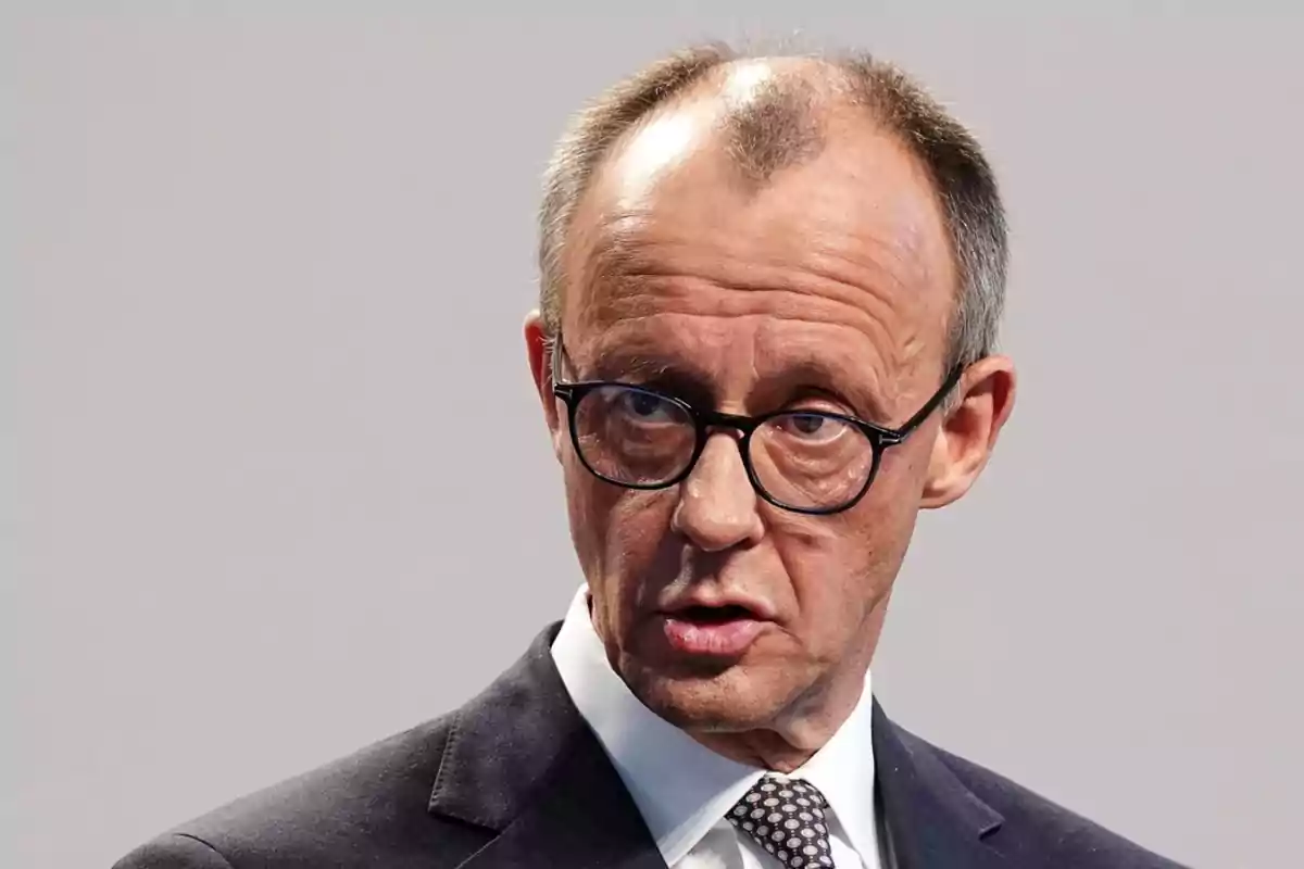 Un hombre con gafas y traje oscuro hablando en un evento.