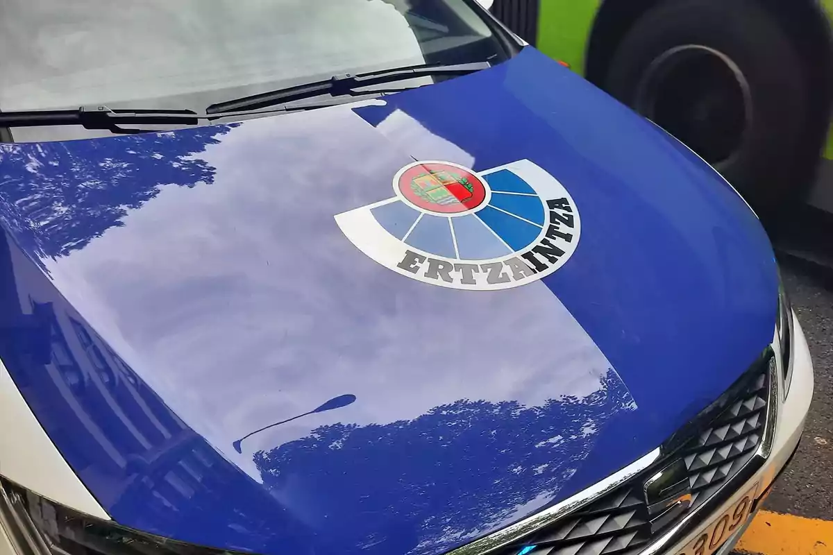 Cofre de un coche patrulla de la Ertzaintza con el escudo visible y reflejo de árboles en la pintura azul