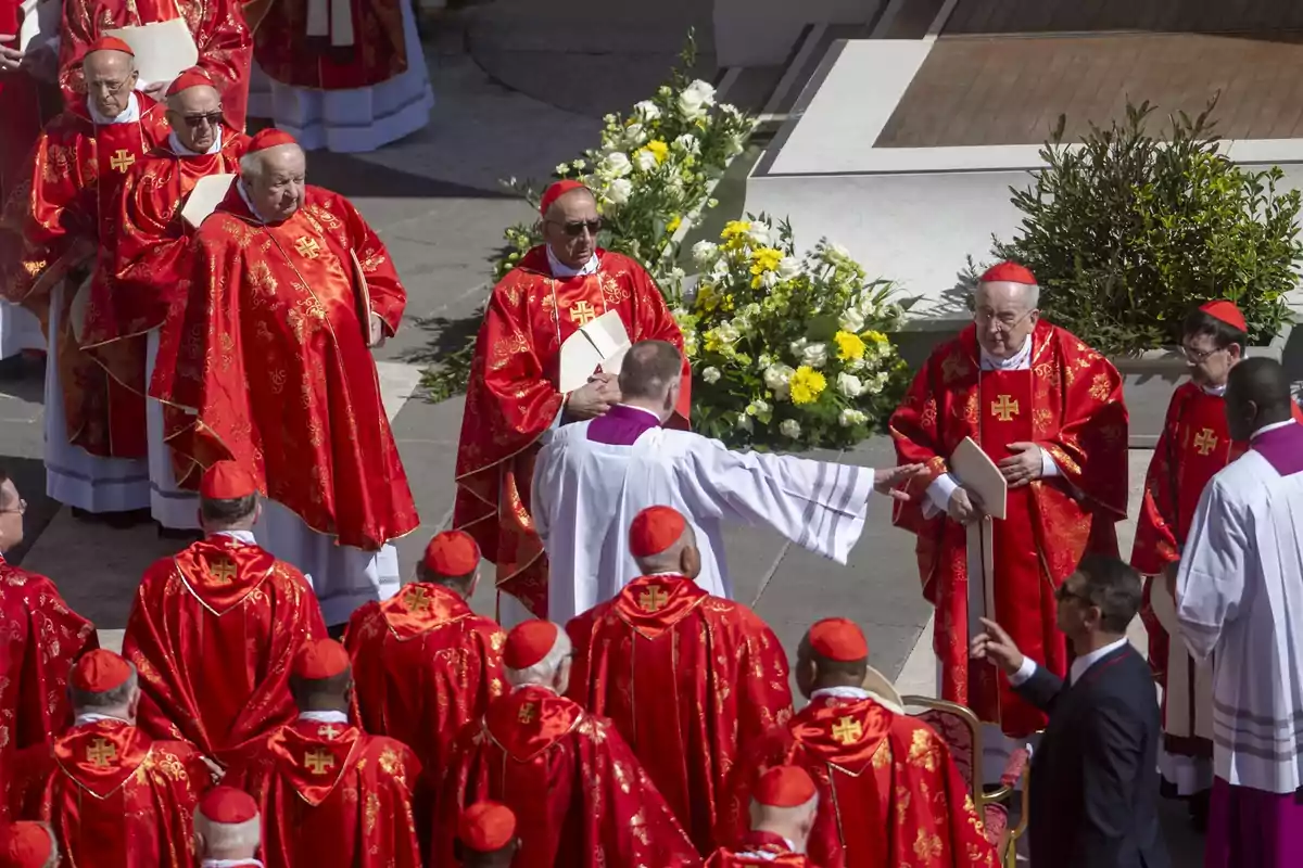 Un grupo de cardenales vestidos con vestimentas rojas se reúne en un evento religioso al aire libre, rodeados de flores y acompañados por otros clérigos. Un grupo de cardenales vestidos con vestimentas rojas se reúne en un evento religioso al aire libre, rodeados de flores y acompañados por otros clérigos.