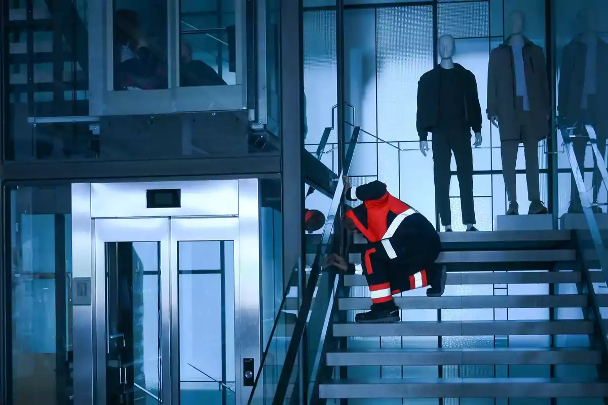 Un trabajador con uniforme de seguridad revisa una escalera en un edificio moderno con maniquíes al fondo.