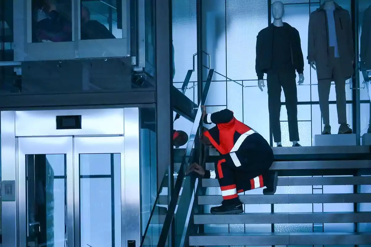 Una persona con uniforme de seguridad revisa una escalera junto a un ascensor y maniquíes en un edificio moderno. Una persona con uniforme de seguridad revisa una escalera junto a un ascensor y maniquíes en un edificio moderno.