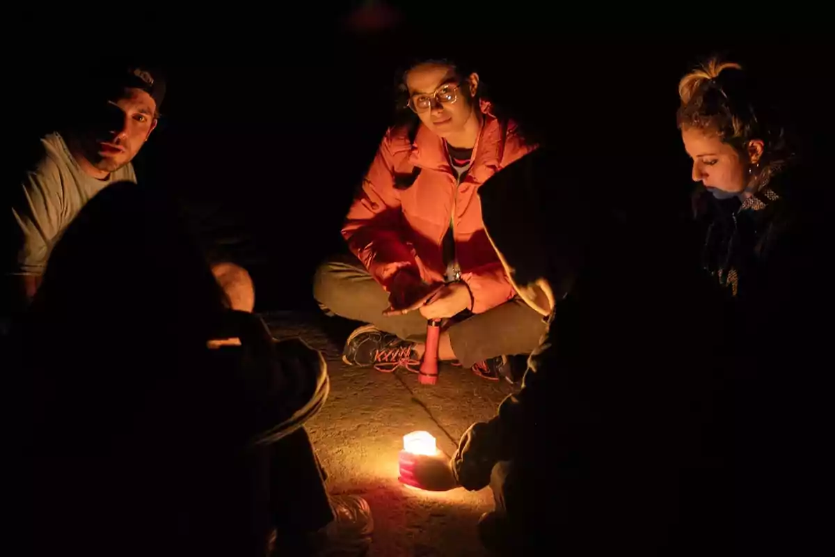 Un grupo de personas sentadas en círculo alrededor de una vela encendida en la oscuridad.