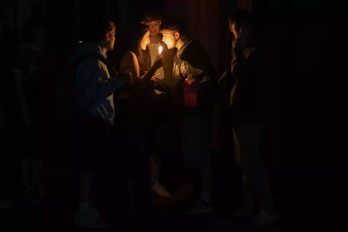 Un grupo de personas se reúne en la oscuridad, iluminados por la luz de una vela.