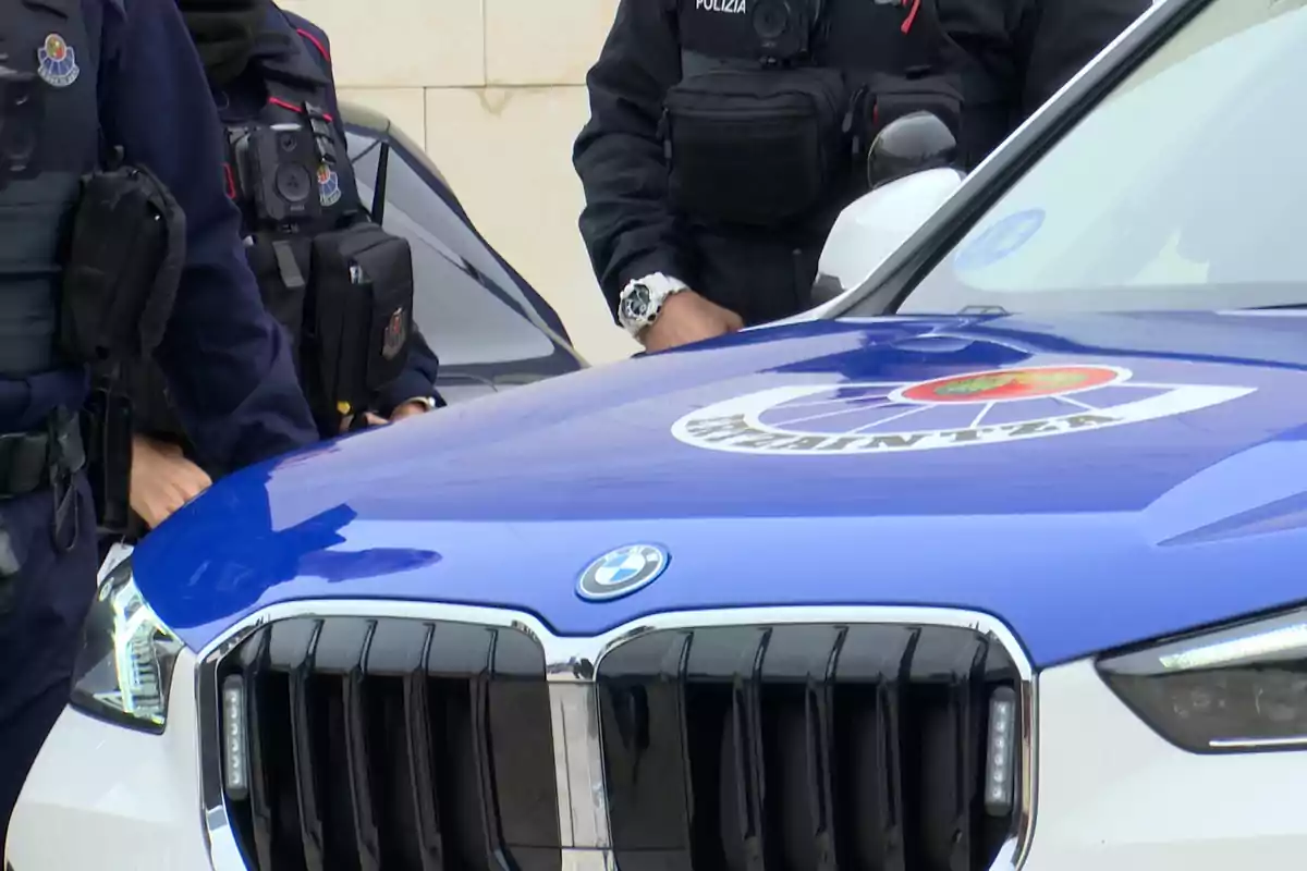 Policías uniformados junto a un coche patrulla BMW con el logo de la policía en el capó Policías uniformados junto a un coche patrulla BMW con el logo de la policía en el capó