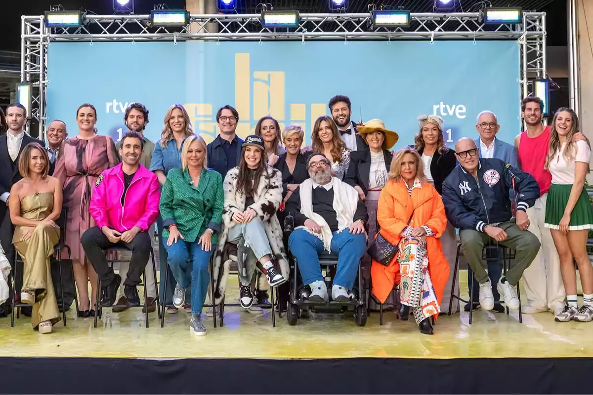 Un grupo numeroso de personas posando sonrientes frente a un fondo azul con el logo de RTVE, algunas sentadas y otras de pie, en un ambiente de evento o presentación Un grupo numeroso de personas posando sonrientes frente a un fondo azul con el logo de RTVE, algunas sentadas y otras de pie, en un ambiente de evento o presentación
