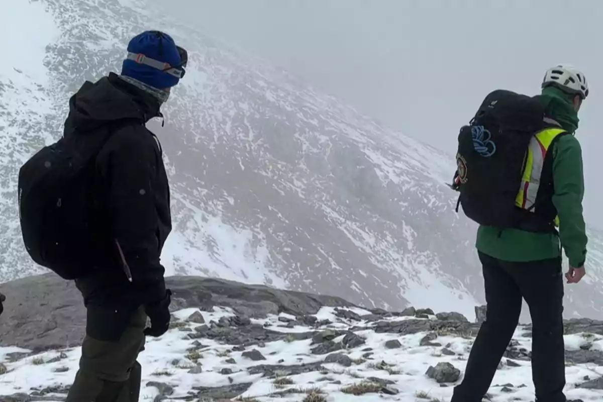 Dos personas con equipo de senderismo y mochilas caminan en un paisaje montañoso nevado. Dos personas con equipo de senderismo y mochilas caminan en un paisaje montañoso nevado.