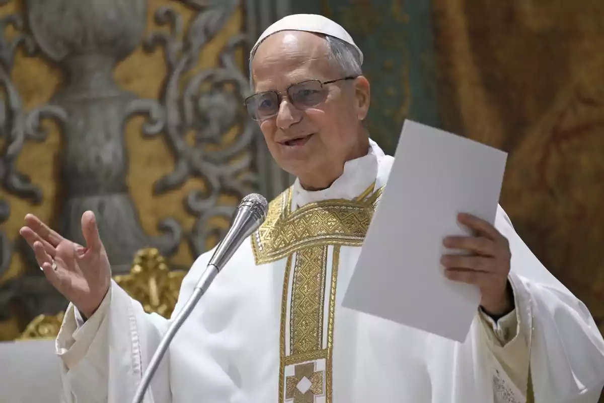 Un hombre con vestimenta religiosa blanca y dorada sostiene un papel mientras habla frente a un micrófono.