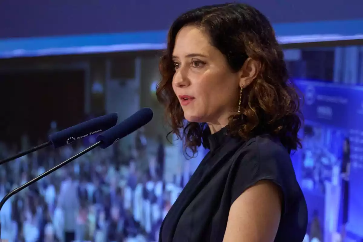 Mujer hablando en un evento con micrófonos frente a ella.