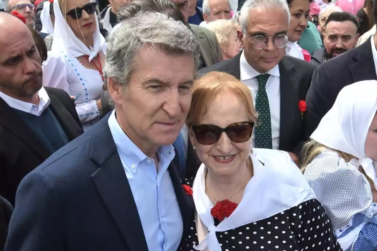 Un grupo de personas, algunas con trajes tradicionales y flores rojas, se encuentra reunido al aire libre en un evento. Un grupo de personas, algunas con trajes tradicionales y flores rojas, se encuentra reunido al aire libre en un evento.