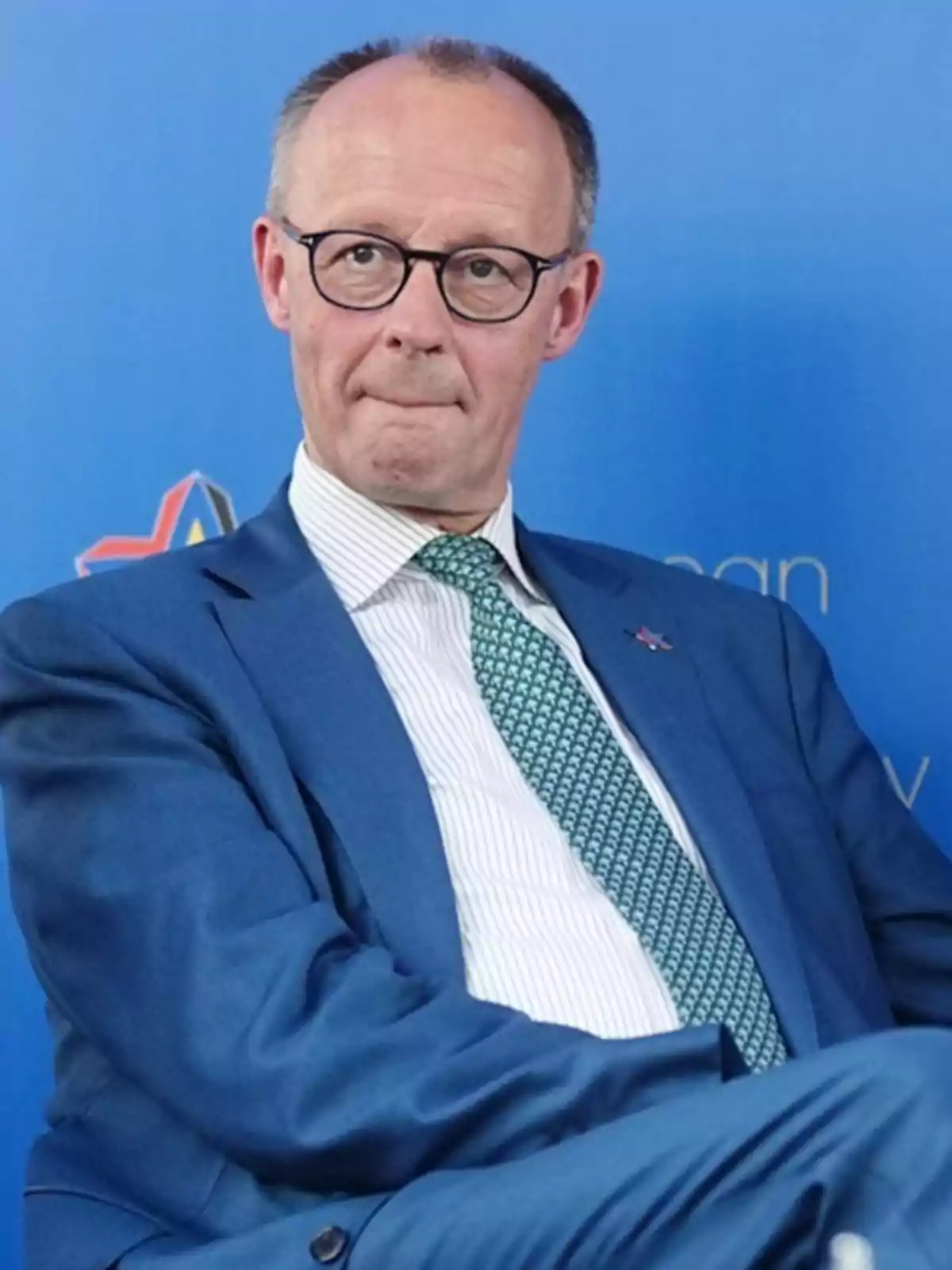Un hombre con gafas y traje azul sentado frente a un fondo azul. Un hombre con gafas y traje azul sentado frente a un fondo azul.