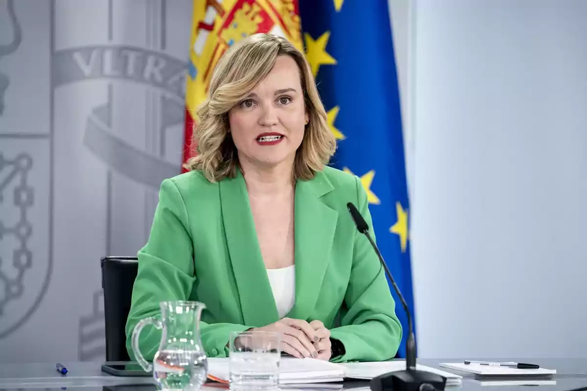 Una mujer con chaqueta verde habla en una conferencia de prensa con banderas de España y la Unión Europea de fondo. Una mujer con chaqueta verde habla en una conferencia de prensa con banderas de España y la Unión Europea de fondo.