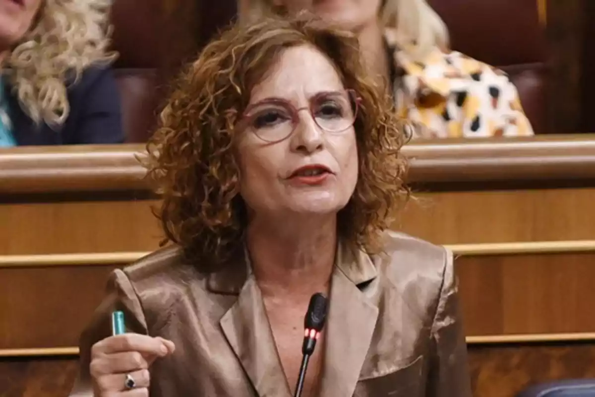 Mujer de cabello rizado y gafas hablando en un micrófono en un entorno parlamentario Mujer de cabello rizado y gafas hablando en un micrófono en un entorno parlamentario