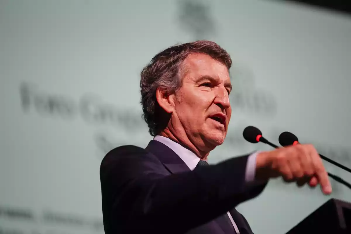 Hombre de mediana edad hablando en un podio con dos micrófonos y fondo desenfocado de letras