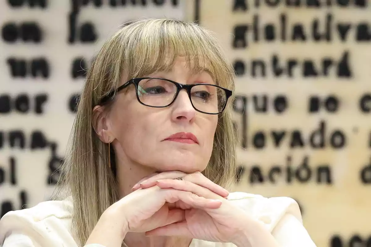 Una persona con gafas y expresión pensativa, con un fondo de texto desenfocado. Una persona con gafas y expresión pensativa, con un fondo de texto desenfocado.
