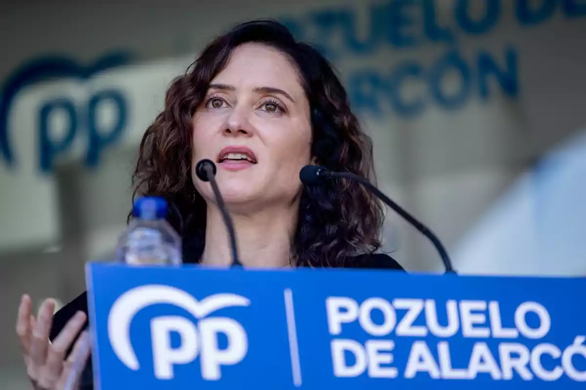 Una persona hablando en un podio con un cartel azul que dice "Pozuelo de Alarcón" y el logo del PP.