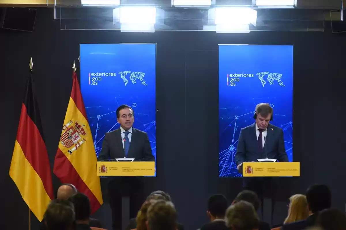 Dos hombres de traje en un podio durante una conferencia de prensa con las banderas de Alemania y España y pantallas azules de fondo con el logo de exteriores gob es Dos hombres de traje en un podio durante una conferencia de prensa con las banderas de Alemania y España y pantallas azules de fondo con el logo de exteriores gob es