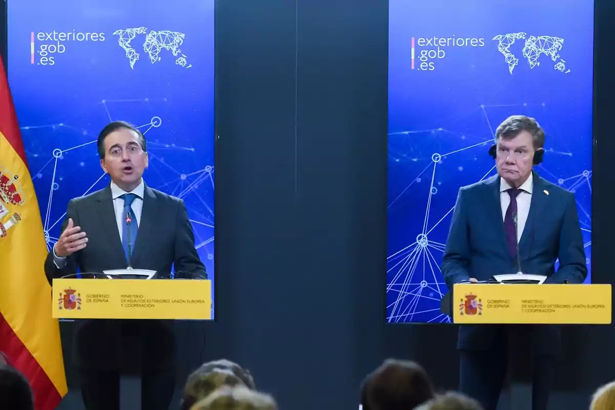 Dos hombres con traje y corbata están de pie en atriles durante una conferencia de prensa frente a pantallas azules con gráficos de redes y el logotipo del Ministerio de Asuntos Exteriores de España Dos hombres con traje y corbata están de pie en atriles durante una conferencia de prensa frente a pantallas azules con gráficos de redes y el logotipo del Ministerio de Asuntos Exteriores de España