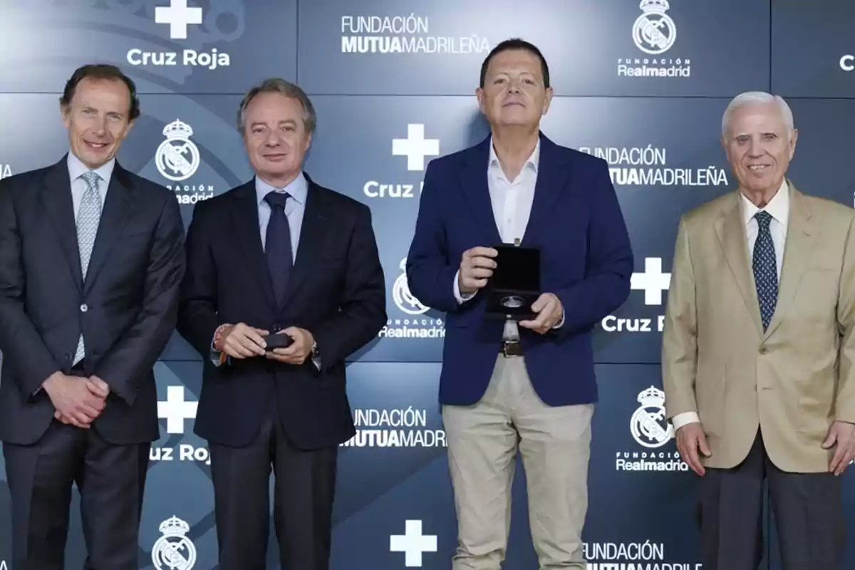 Cuatro hombres posan de pie en un evento formal con fondo de logotipos de la Cruz Roja, Fundación Mutua Madrileña y Fundación Real Madrid, dos de ellos sostienen una caja de reconocimiento Cuatro hombres posan de pie en un evento formal con fondo de logotipos de la Cruz Roja, Fundación Mutua Madrileña y Fundación Real Madrid, dos de ellos sostienen una caja de reconocimiento