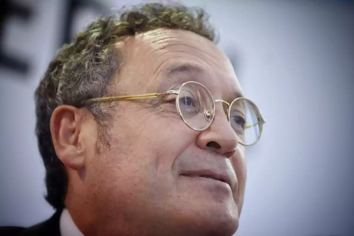 Hombre de cabello rizado y gafas redondas doradas mirando hacia un lado con expresión sonriente