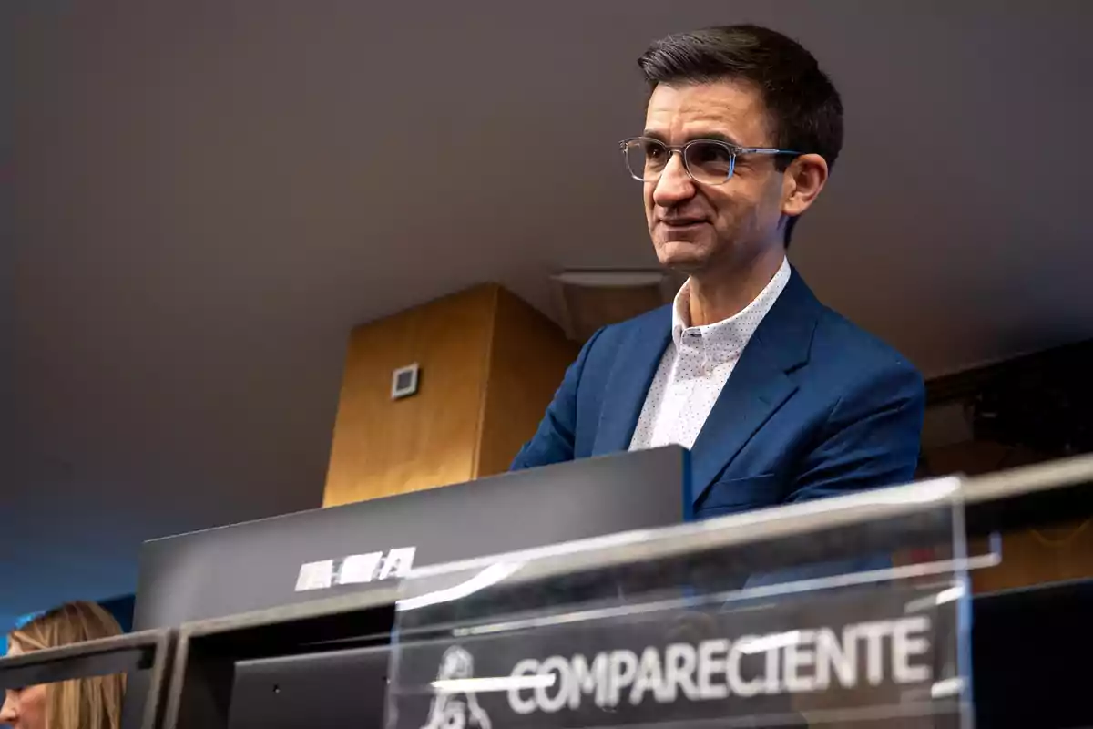 Hombre con gafas y saco azul hablando en una comparecencia en un entorno institucional Hombre con gafas y saco azul hablando en una comparecencia en un entorno institucional