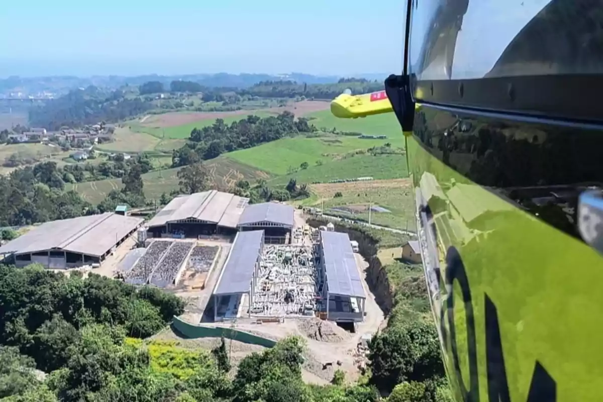 Vista aérea de una planta industrial rodeada de áreas verdes y campos, tomada desde un helicóptero en vuelo.