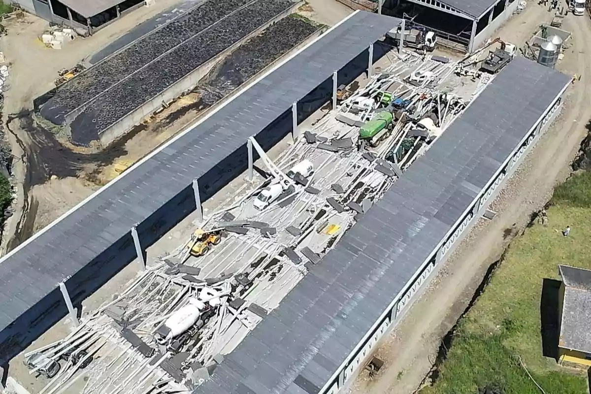 Vista aérea de una nave industrial con el techo colapsado y varios vehículos atrapados entre los escombros Vista aérea de una nave industrial con el techo colapsado y varios vehículos atrapados entre los escombros