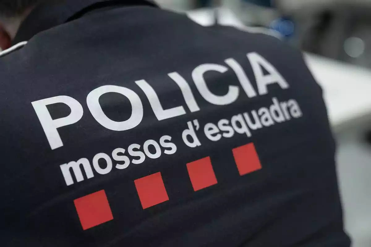 Espalda de un uniforme de los Mossos d'Esquadra con el texto policía y cuatro cuadros rojos