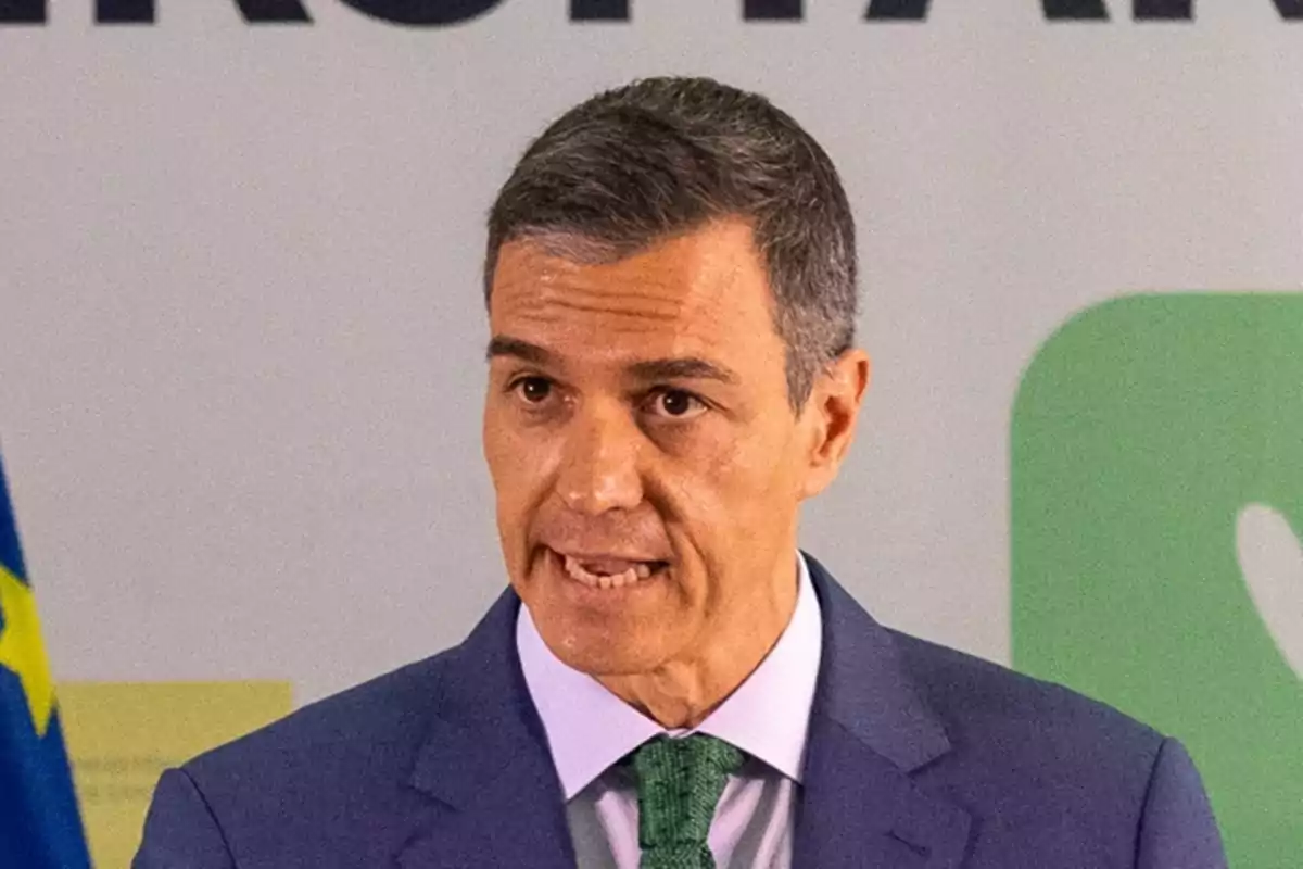 Hombre de cabello corto y canoso con traje azul y corbata verde hablando frente a un micrófono Hombre de cabello corto y canoso con traje azul y corbata verde hablando frente a un micrófono