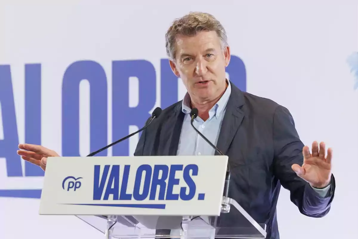 Hombre de cabello canoso hablando en un atril con el cartel de un partido político que dice VALORES Hombre de cabello canoso hablando en un atril con el cartel de un partido político que dice VALORES