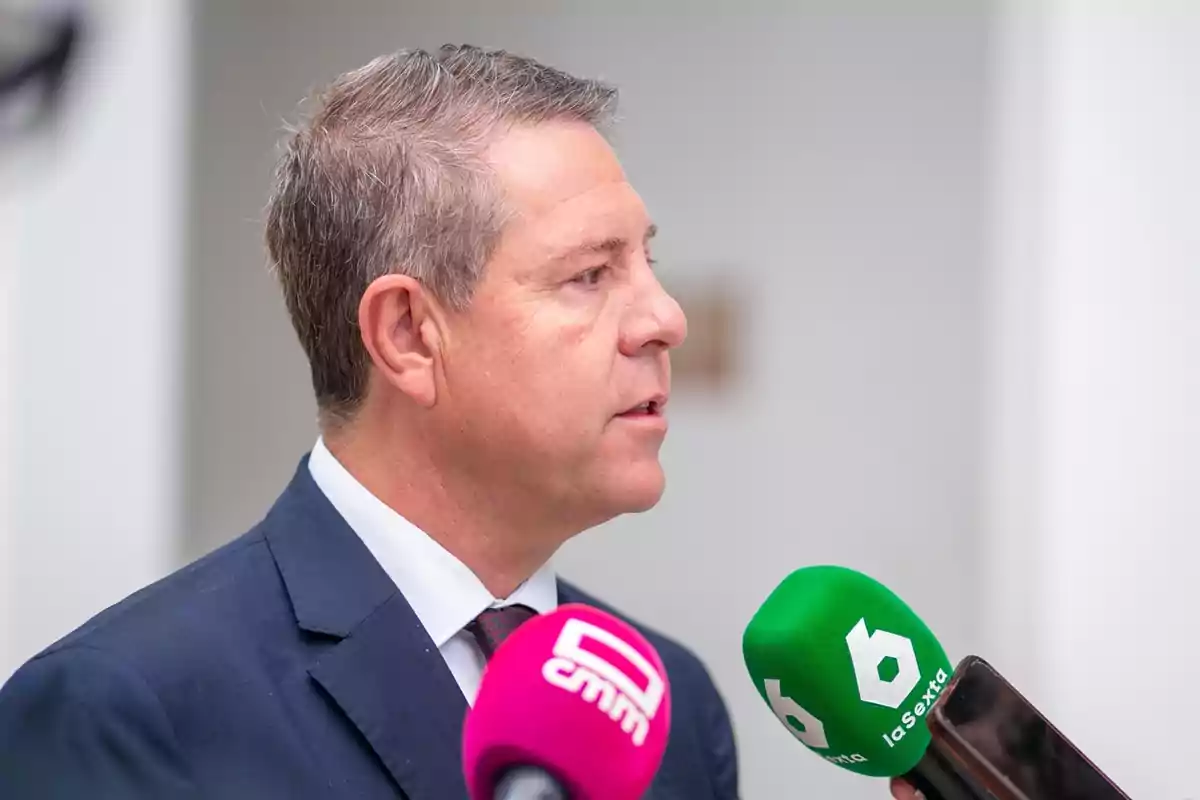 Hombre de traje dando declaraciones a la prensa frente a micrófonos de medios de comunicación Hombre de traje dando declaraciones a la prensa frente a micrófonos de medios de comunicación