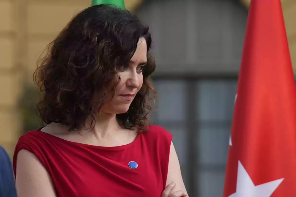 Mujer de cabello rizado y vestido rojo mirando hacia abajo junto a una bandera roja con estrellas blancas