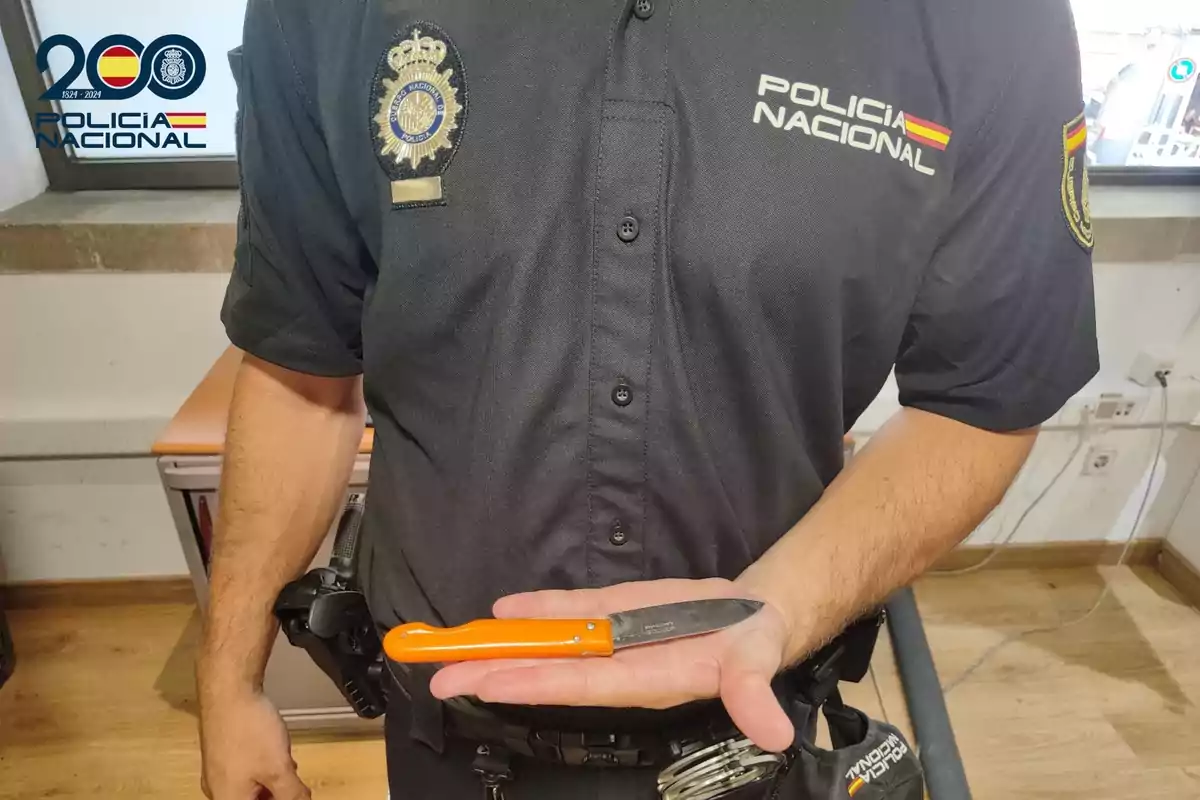 Agente de la Policía Nacional sostiene un cuchillo de mango naranja en la palma de su mano dentro de una oficina Agente de la Policía Nacional sostiene un cuchillo de mango naranja en la palma de su mano dentro de una oficina