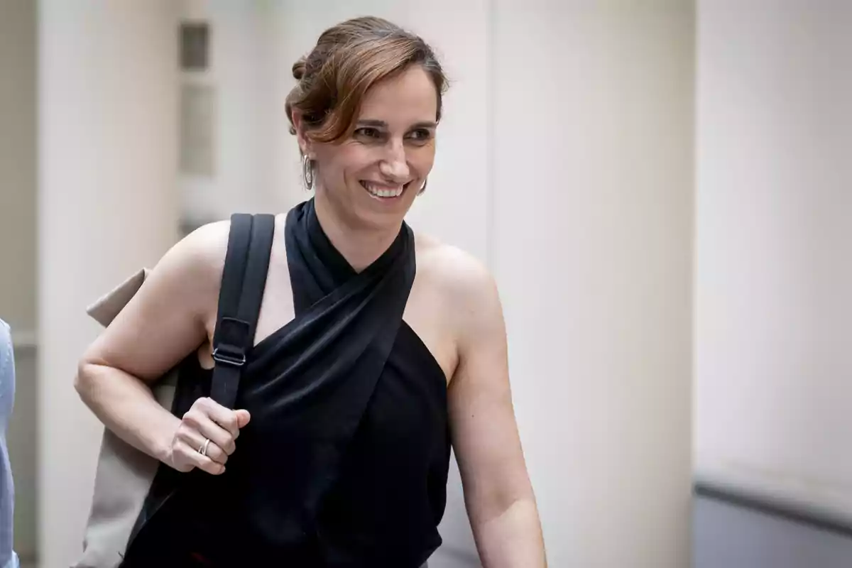 Mujer sonriente con blusa negra de tirantes y bolso al hombro caminando en un espacio interior iluminado