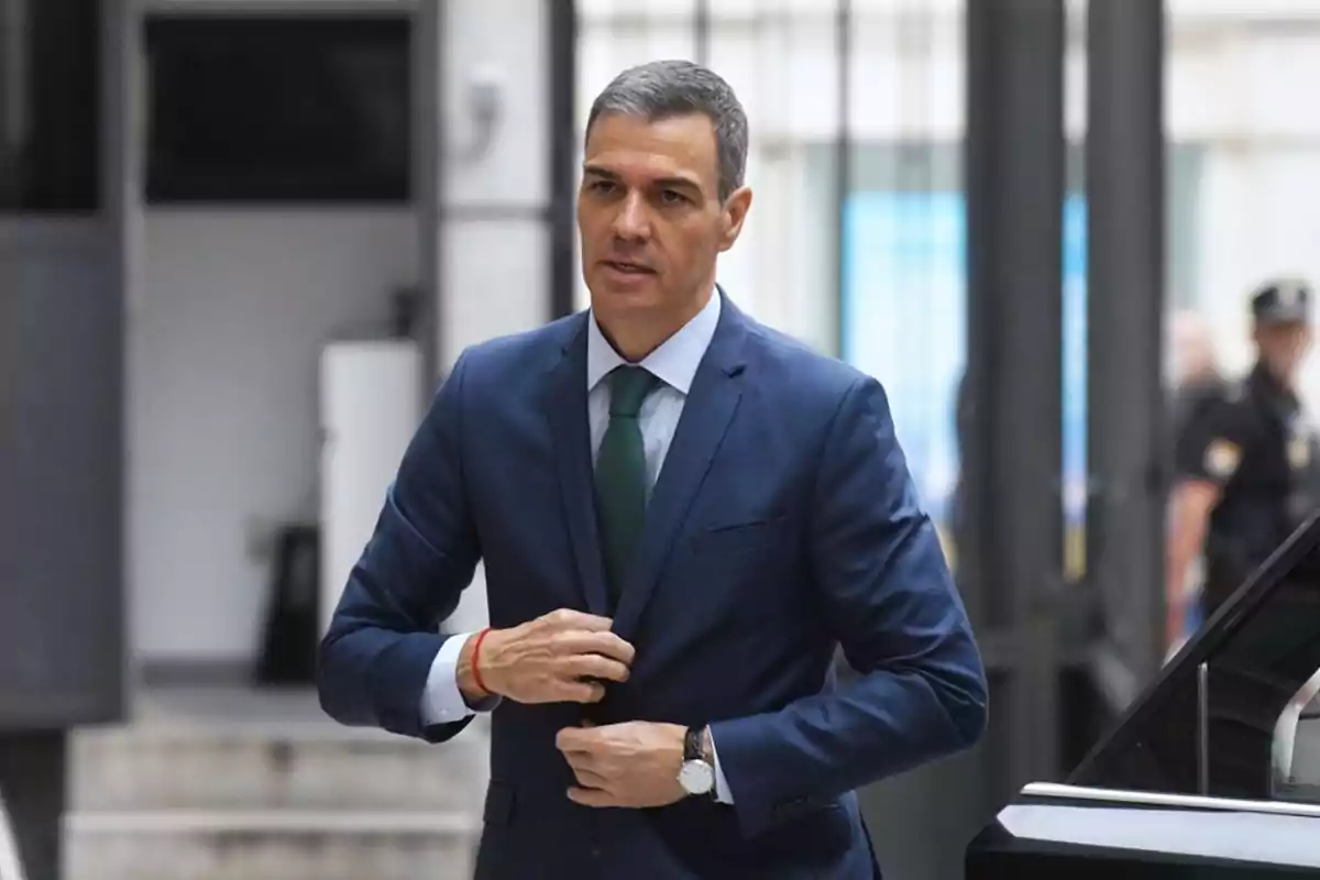 Hombre con traje azul y corbata verde abrochándose el saco mientras camina junto a un automóvil en un entorno urbano Hombre con traje azul y corbata verde abrochándose el saco mientras camina junto a un automóvil en un entorno urbano