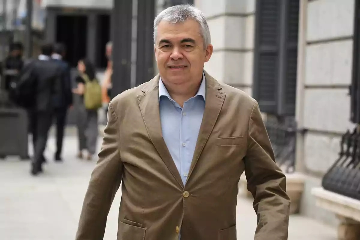 Hombre de cabello canoso con saco marrón y camisa azul caminando por una calle urbana