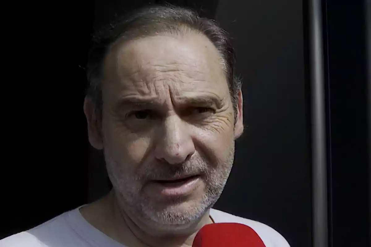 Hombre de mediana edad con barba y cabello corto sosteniendo un micrófono rojo frente a él Hombre de mediana edad con barba y cabello corto sosteniendo un micrófono rojo frente a él