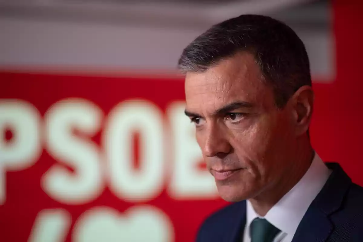 Hombre de cabello corto y canoso con expresión seria frente a un fondo rojo con letras blancas desenfocadas