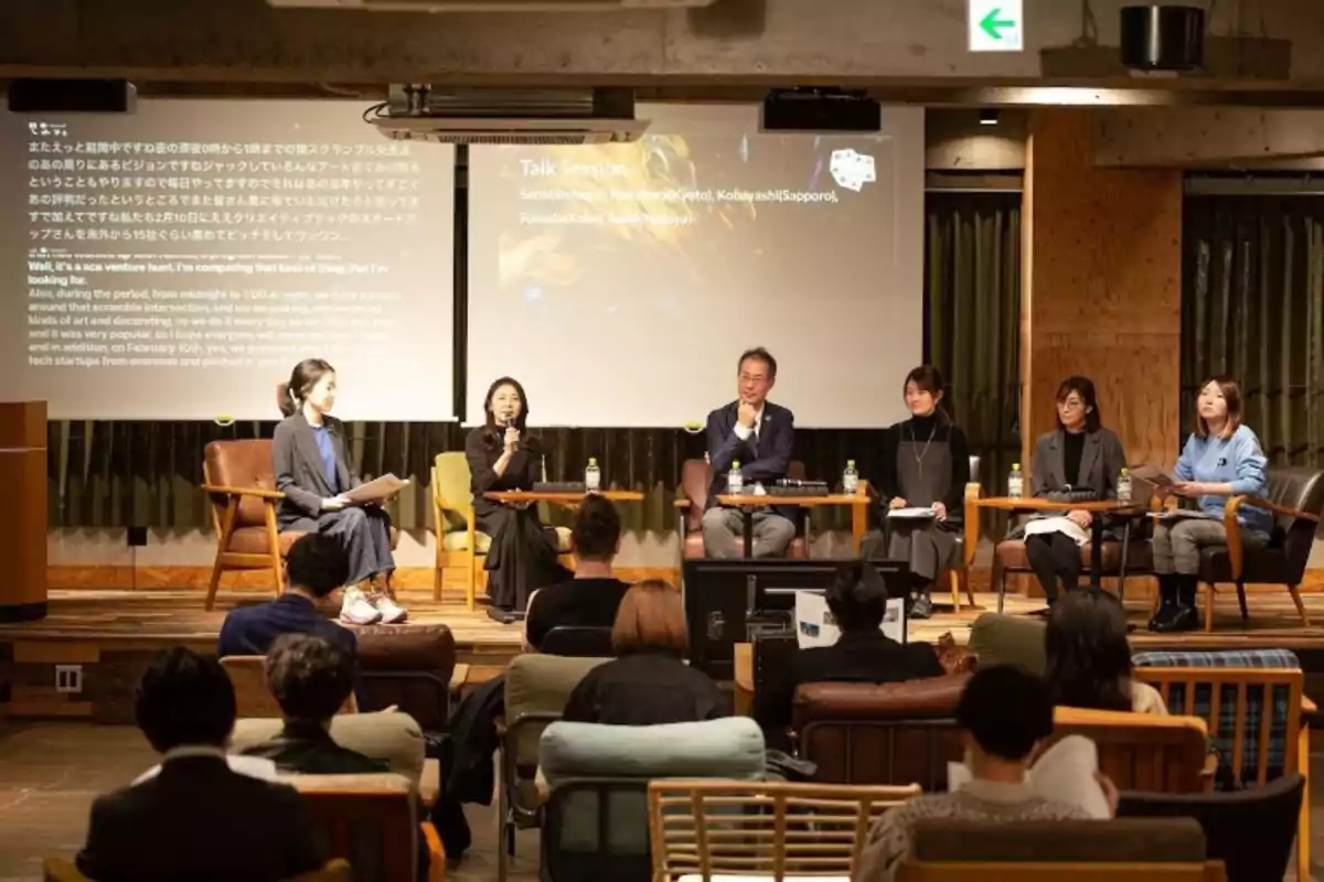 A group of people is participating in a discussion session in an auditorium, with a projector displaying text on the screen behind them.