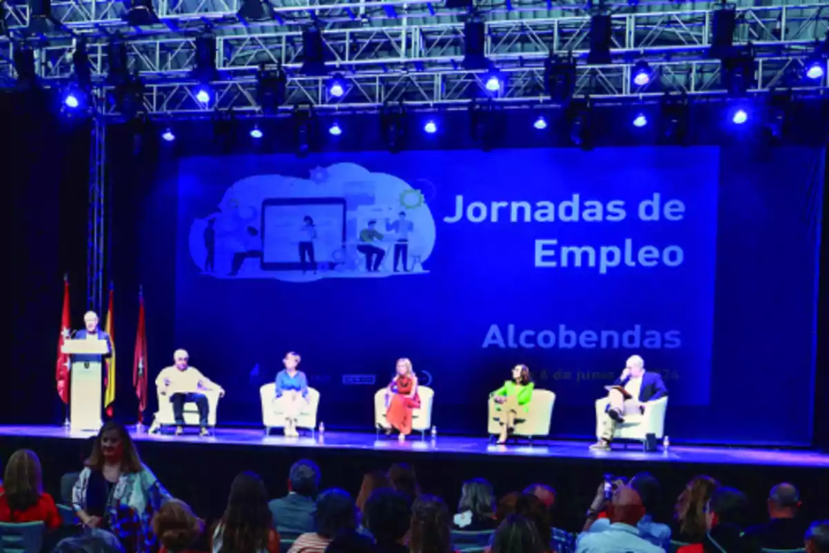 Personas sentadas en un escenario iluminado con luces azules durante las Jornadas de Empleo en Alcobendas.