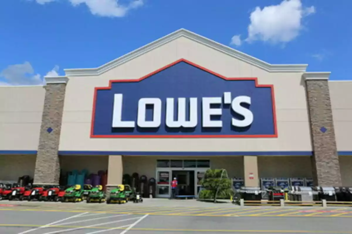 Fachada de una tienda Lowe's con equipos de jardinería en la entrada y cielo azul de fondo. Fachada de una tienda Lowe's con equipos de jardinería en la entrada y cielo azul de fondo.