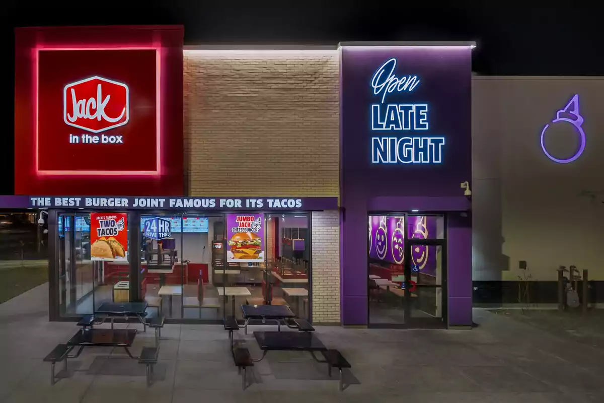 The image shows the facade of a fast-food restaurant with illuminated signs indicating that it is open late and is famous for its tacos.