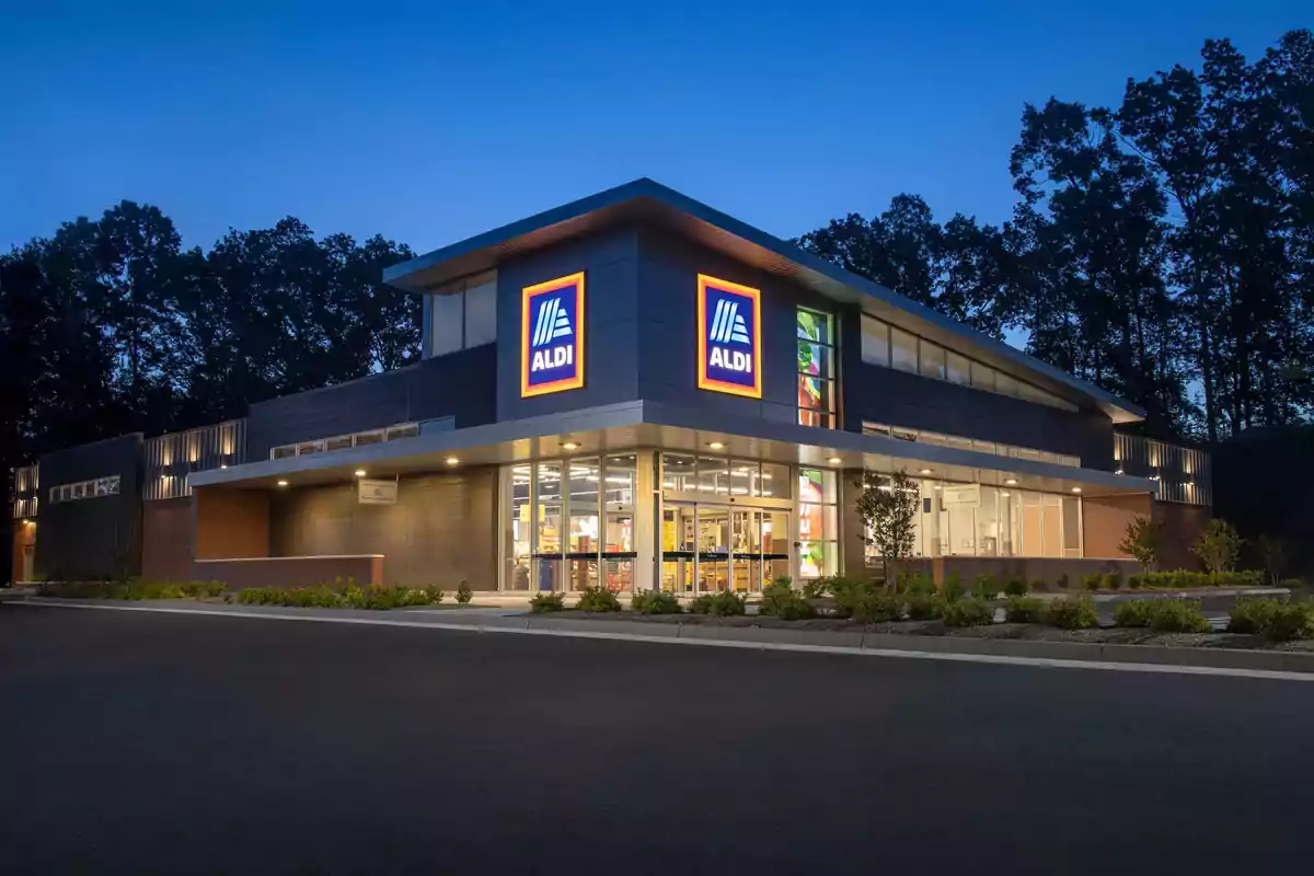 Facade of an ALDI store illuminated at dusk with trees in the background and an empty parking lot in the front Facade of an ALDI store illuminated at dusk with trees in the background and an empty parking lot in the front