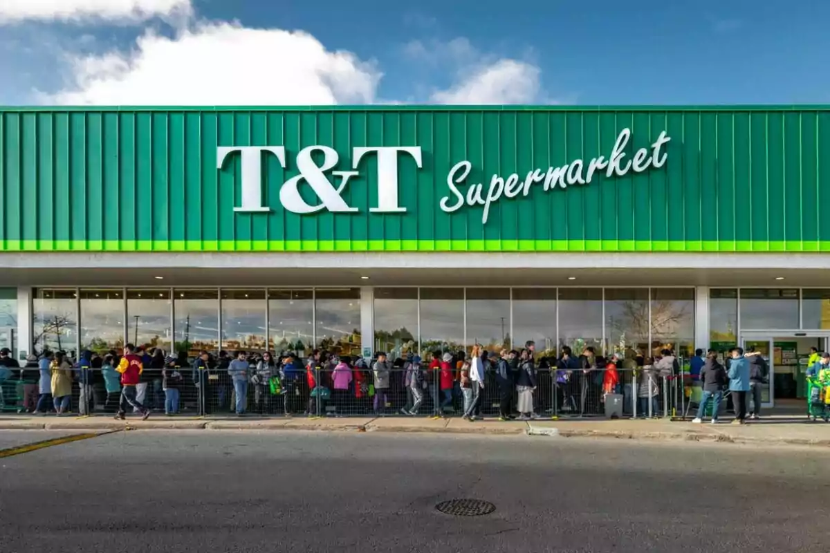 A crowd of people is lining up in front of the entrance of a T&T supermarket with a green and white sign. A crowd of people is lining up in front of the entrance of a T&T supermarket with a green and white sign.